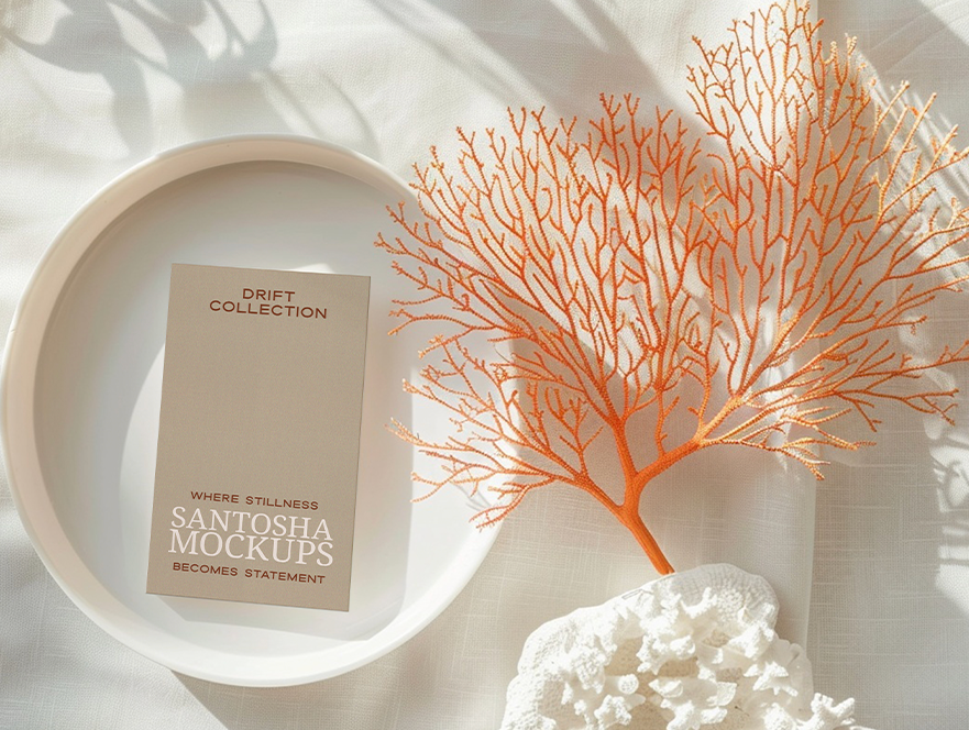 Vertical business card mockup from the DRIFT Collection by Studio Santosha, displayed on a white dish with orange coral and white coral decoration on a soft fabric surface.
