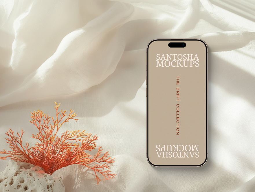 iPhone mockup from the DRIFT Collection by Studio Santosha, displayed on a soft white fabric surface with coral decoration and natural stone detail.