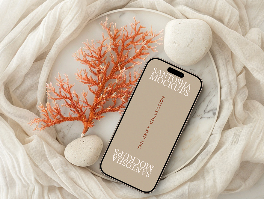 iPhone mockup from the DRIFT Collection by Studio Santosha, styled on a marble surface with coral decoration, natural stones, and soft fabric backdrop.
