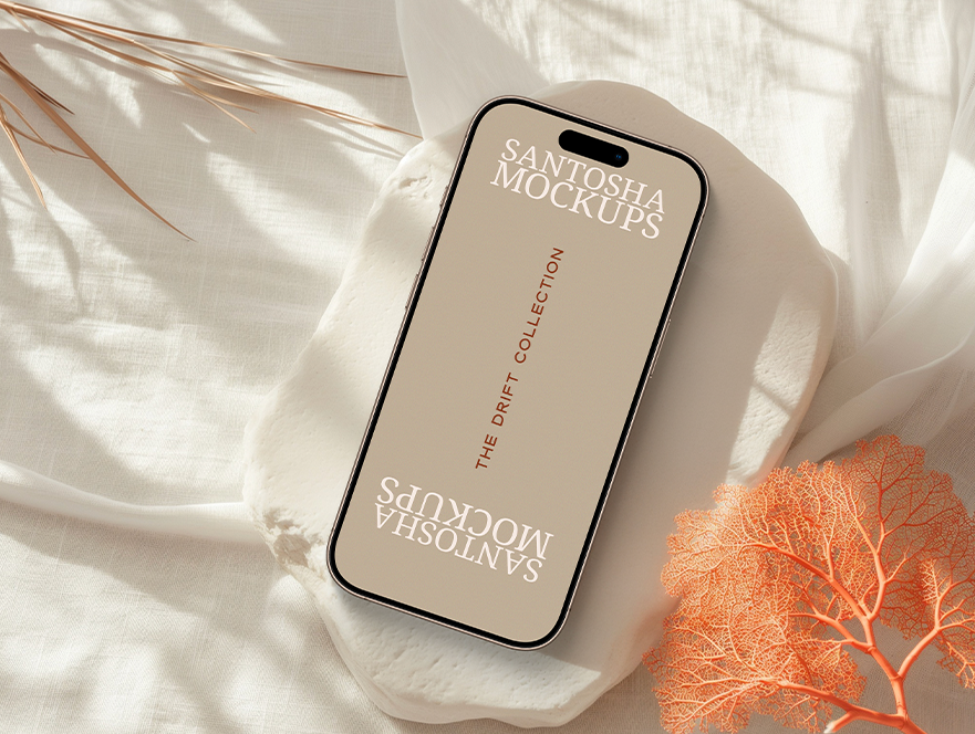 iPhone mockup from the DRIFT Collection by Studio Santosha, styled on a soft fabric surface with coral decoration and natural light shadows.