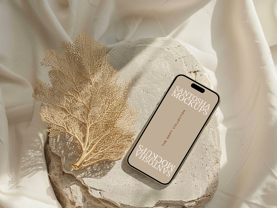 iPhone mockup from the DRIFT Collection by Studio Santosha, styled on a textured stone surface with golden coral leaf decoration and soft fabric backdrop.