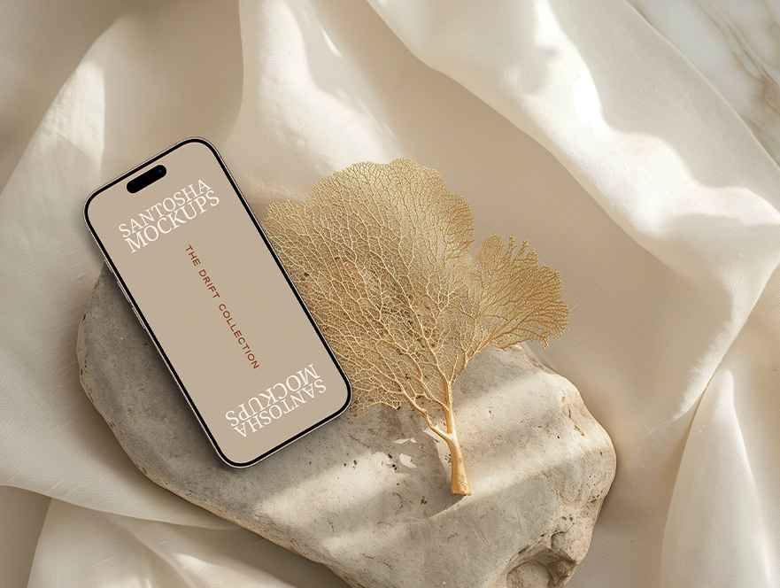 iPhone mockup from the DRIFT Collection by Studio Santosha, displayed on a stone surface with delicate dried golden coral and soft fabric background.