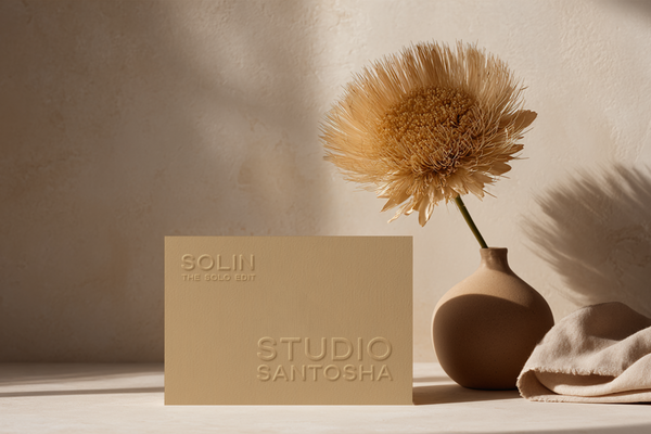 Minimal business card mockup from Studio Santosha’s SOLIN Solo Edit, featuring a beige card with embossed text, a sculptural vase with a dried flower, and soft linen styling in warm natural light.