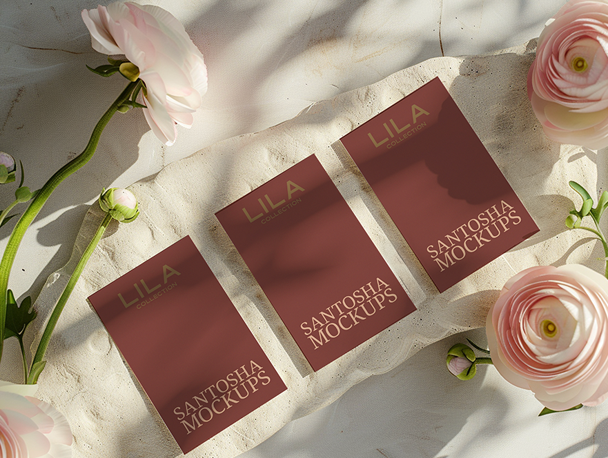 Studio Santosha mockup featuring three LILA business cards arranged on a light textured surface with soft shadows and pink ranunculus flowers surrounding them.