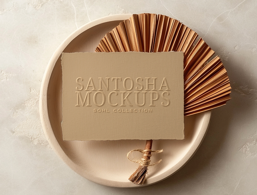 Business card mockup from the SOHL Collection by Studio Santosha — beige embossed card styled on a round ceramic plate with dried fan leaves, set against a neutral background.