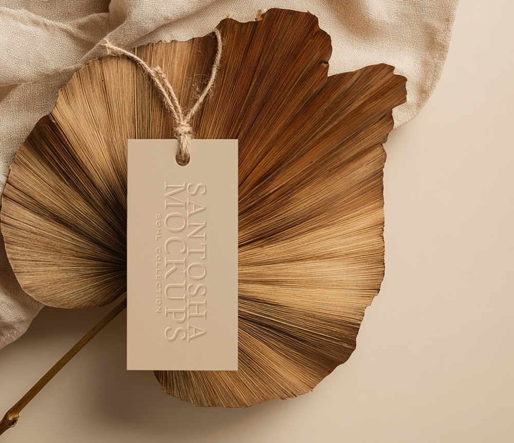 Studio Santosha mockup from the SOHL Collection, showcasing an embossed beige tag with natural rope, styled on a sculptural dried palm leaf and soft linen backdrop in warm neutral tones.
